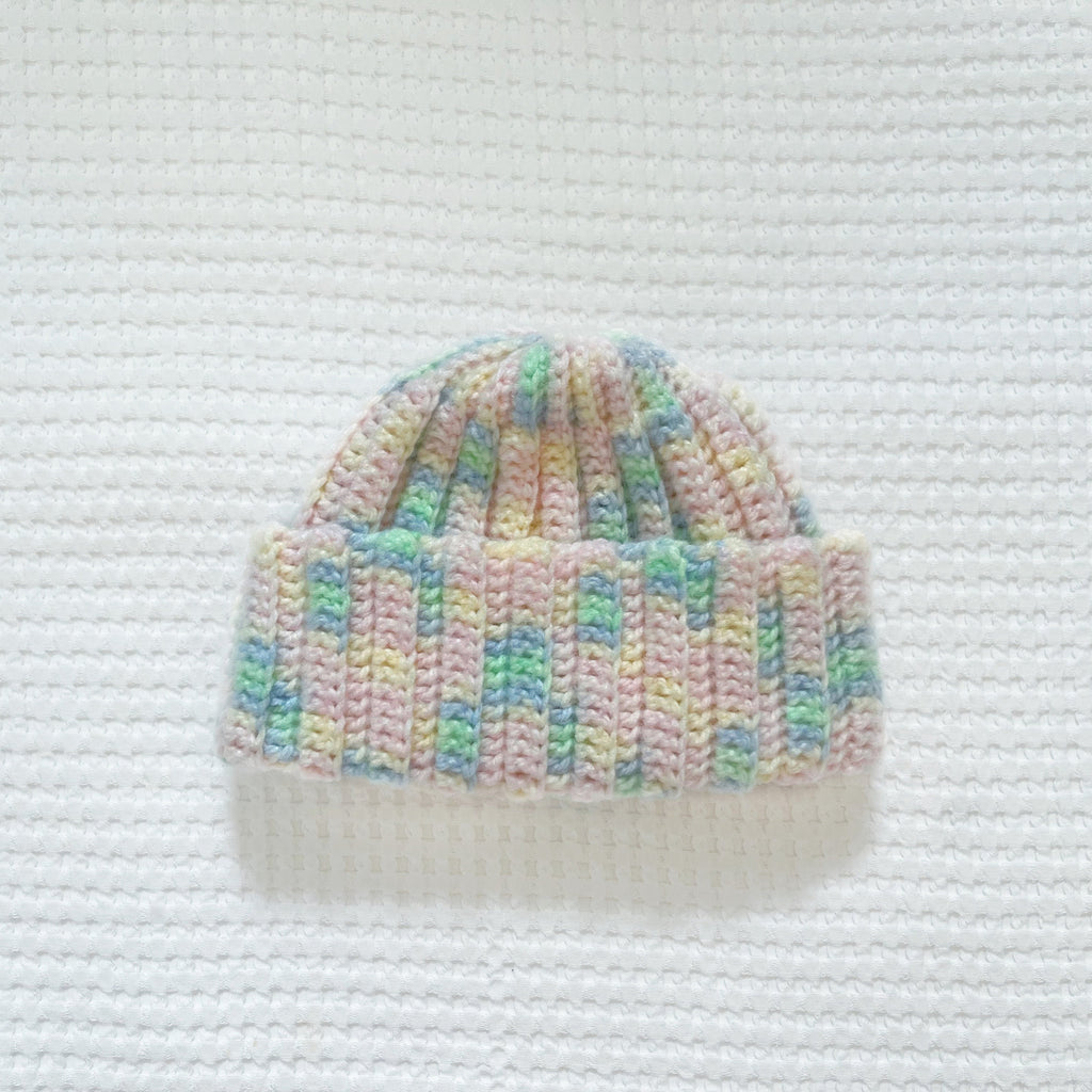 Crochet beanie with pastel colors on a textured white background