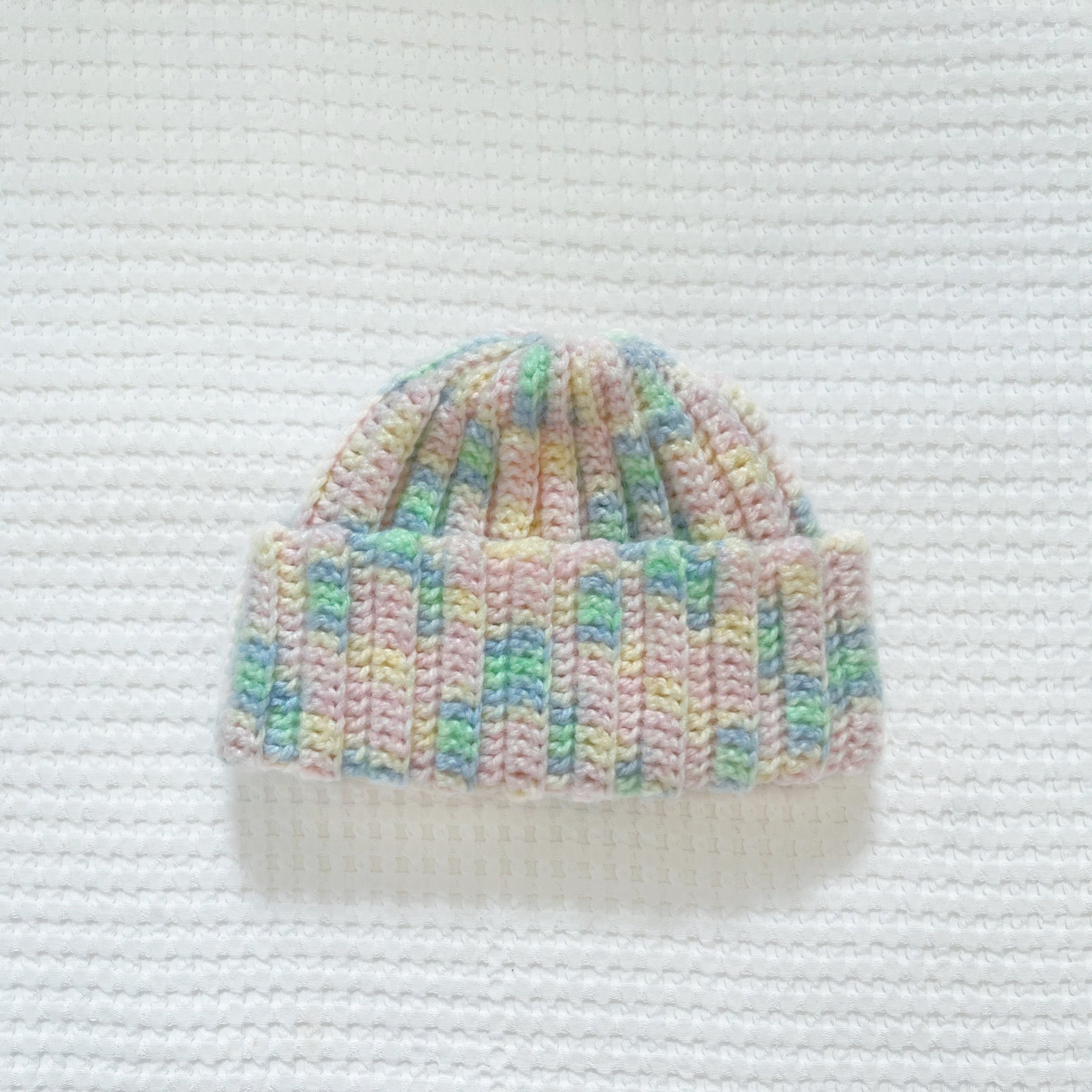 Crochet beanie with pastel colors on a textured white background