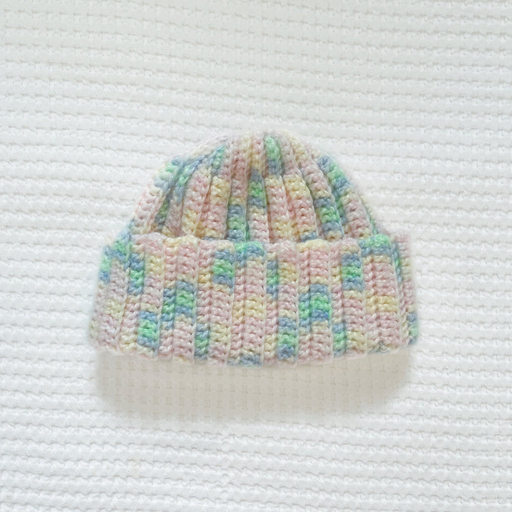Crochet beanie with pastel colors on a white textured background