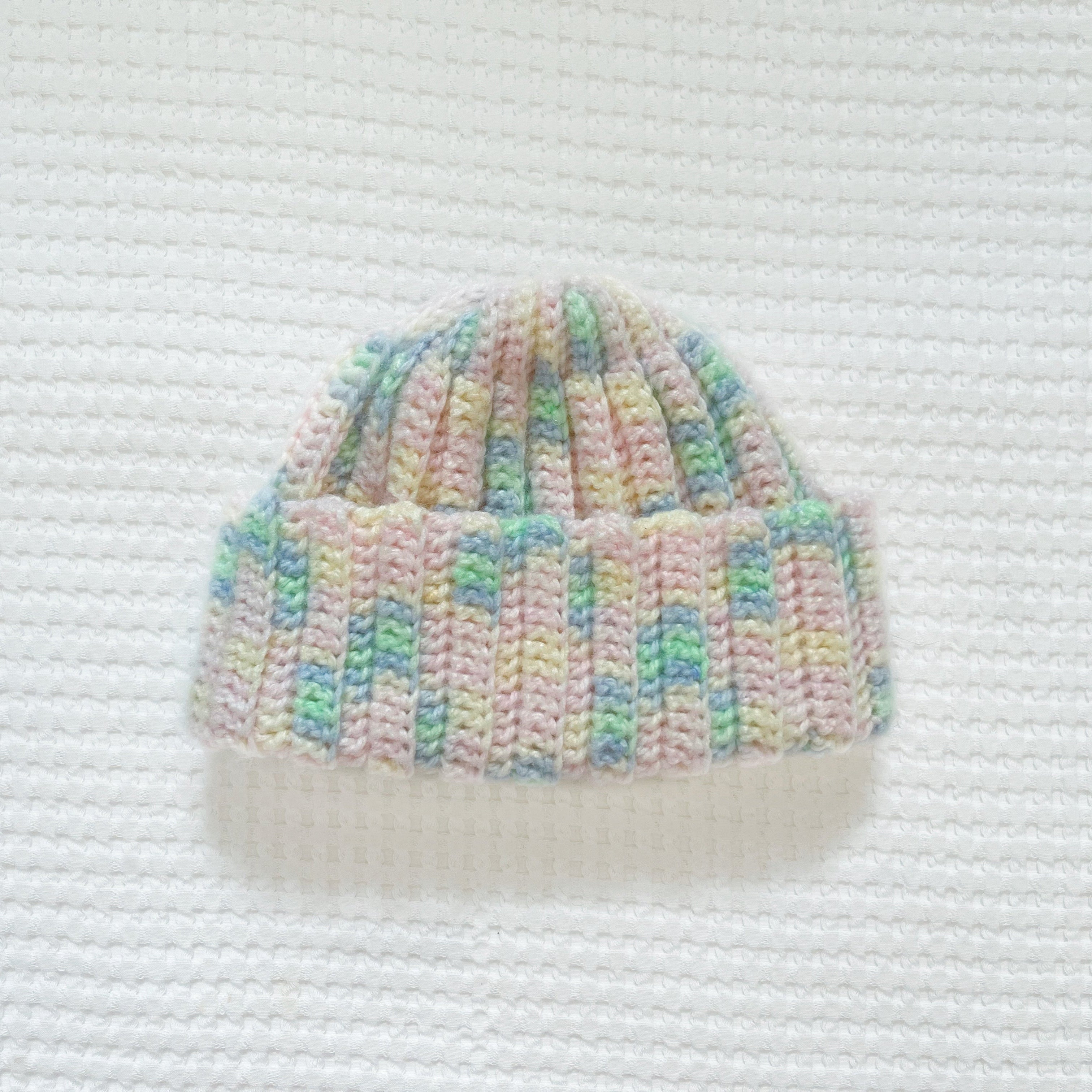 Crochet beanie with pastel colors on a white textured background