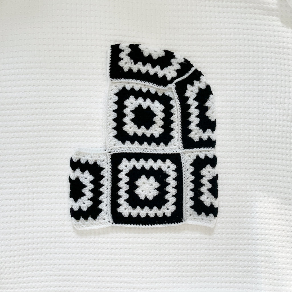 Black and white crocheted balaclava on a textured white background