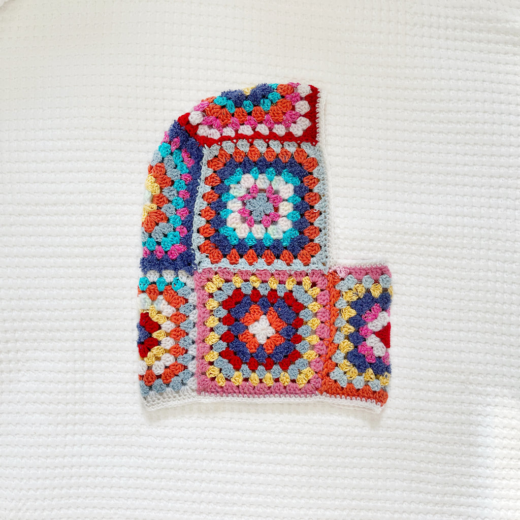 Colorful crocheted balaclava with square patterns on a white background