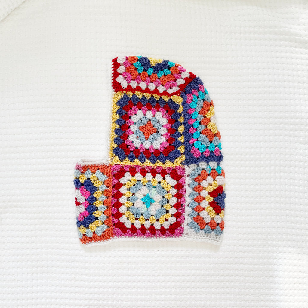 Colorful crocheted balaclava with square patterns on a white background